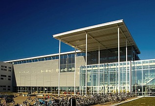 A photograph of the school complex, featuring classrooms spread over three floors, sports facilities and an underground car park and cycle storage area.