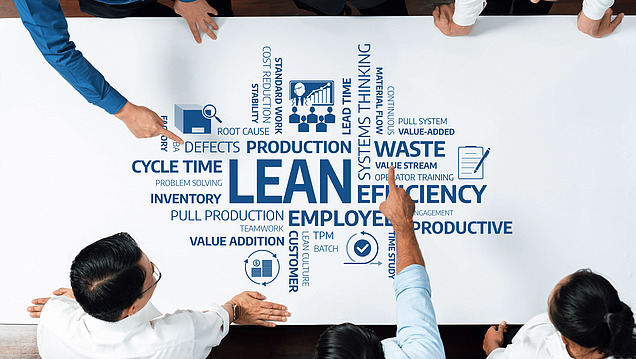 Top-down view of staff looking at a very large LEAN diagram on a table. 