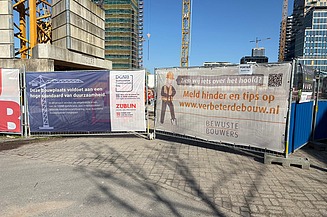 Een foto van een Bewuste Bouwers‑banner op de bouwhekken van project &Amsterdam